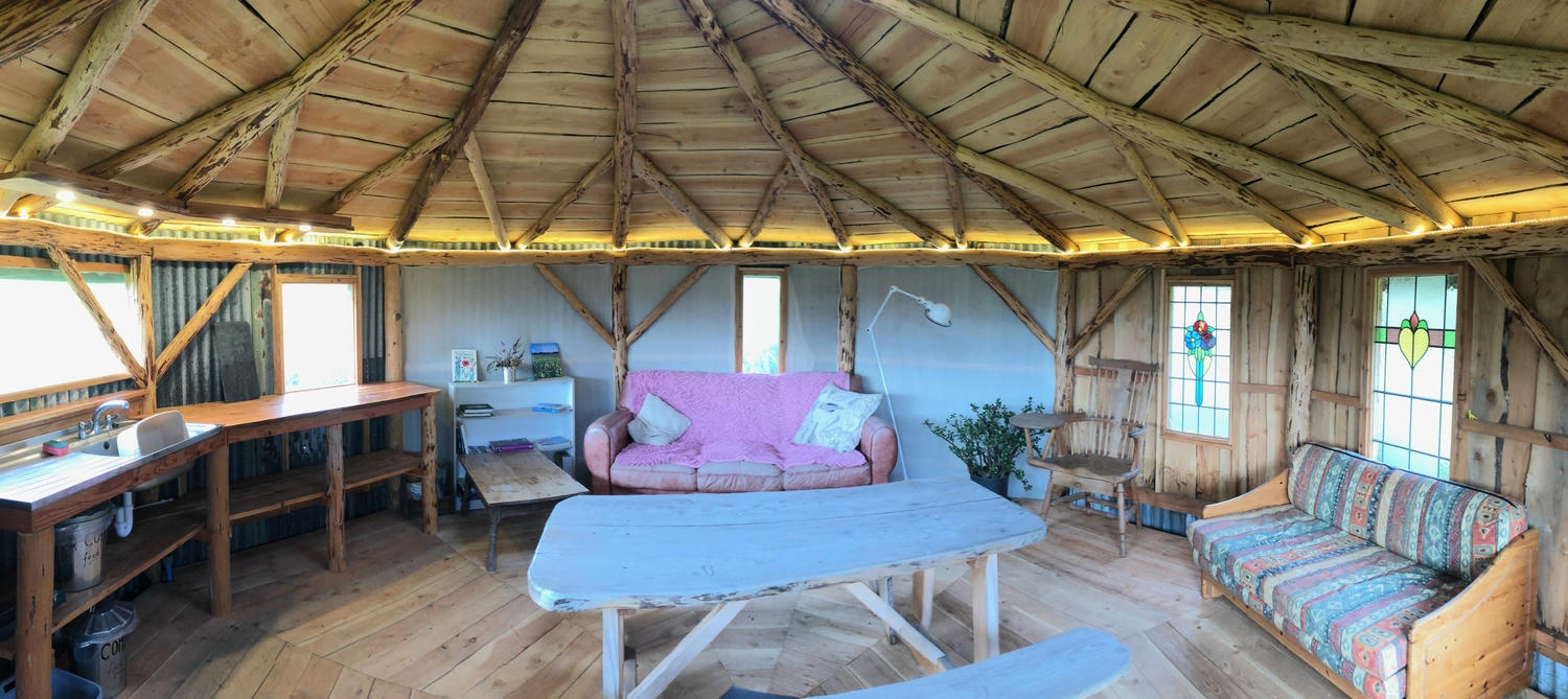 A view of the inside of the larch pole roundhouse, including sofas, sinks, chairs and tables